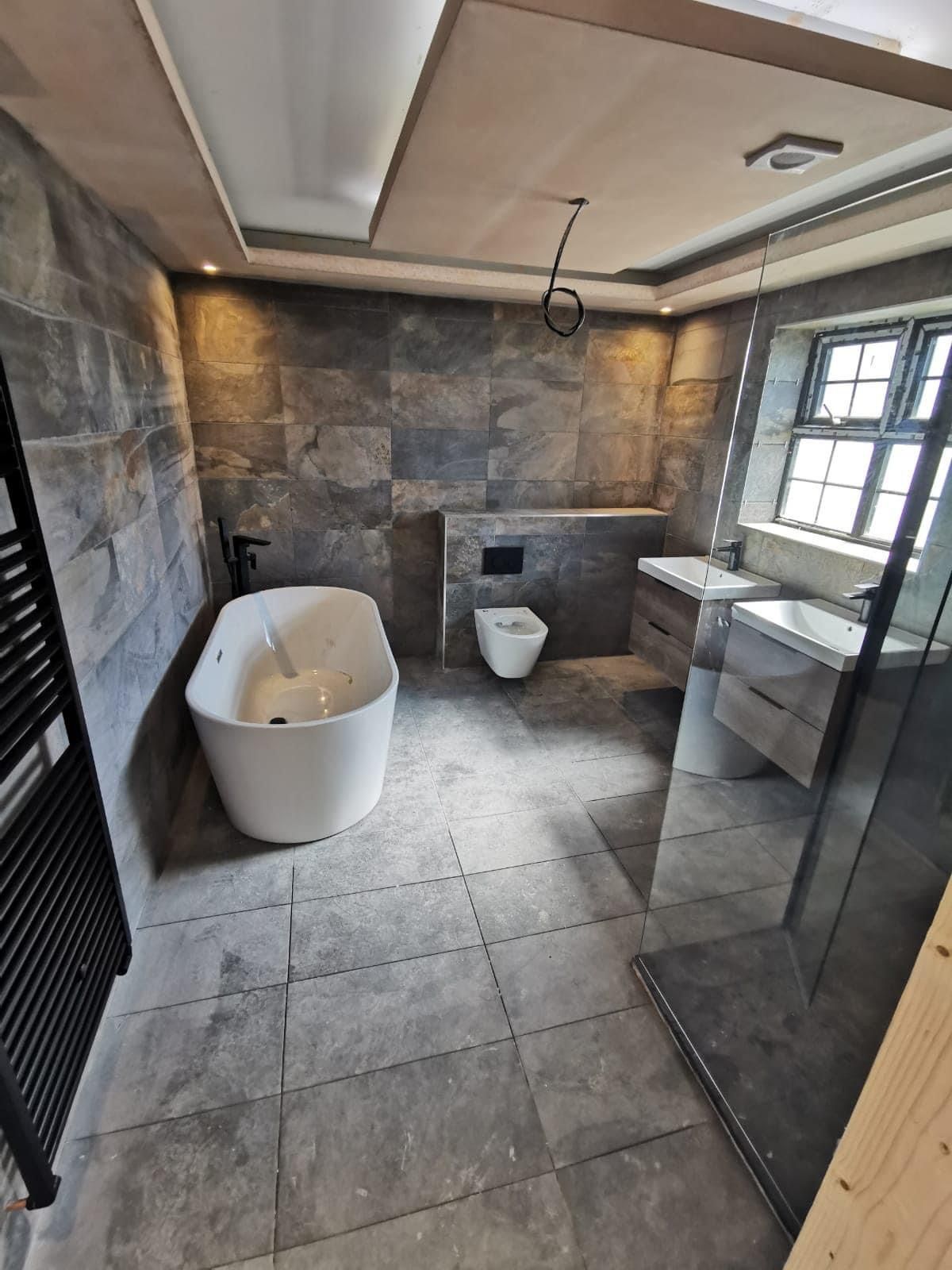 Slate-tiled bathroom with a freestanding bath and a black towel radiator