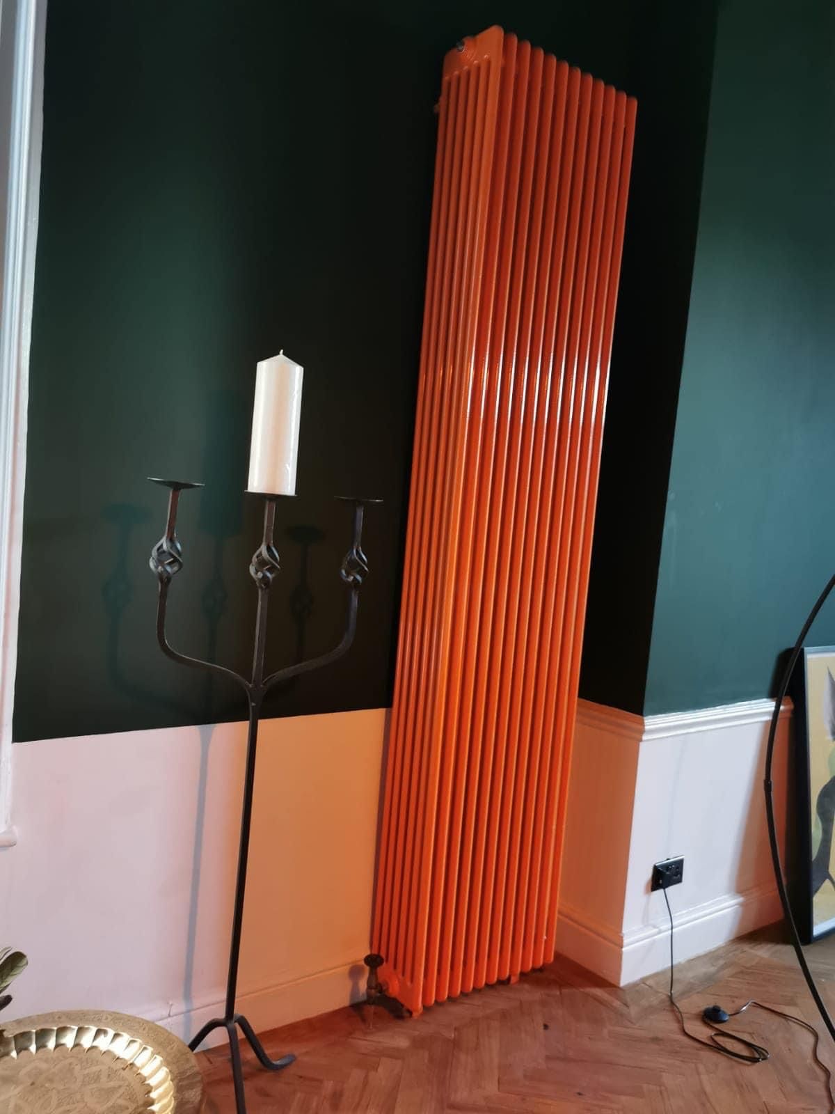 Tall orange column radiator fitted against a dark green wall